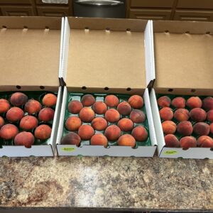 Three boxes of ripe peaches on a kitchen counter.