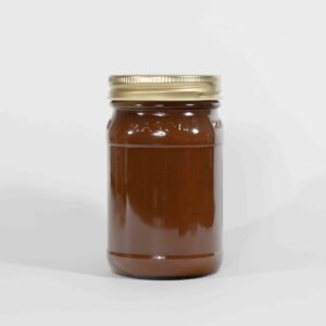 Glass jar filled with brown sauce or spread with a gold lid.