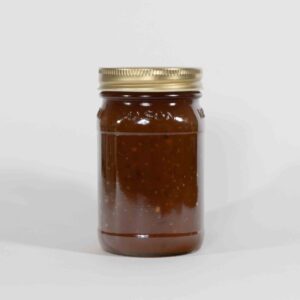 A clear jar filled with dark brown sauce or condiment with a golden lid.